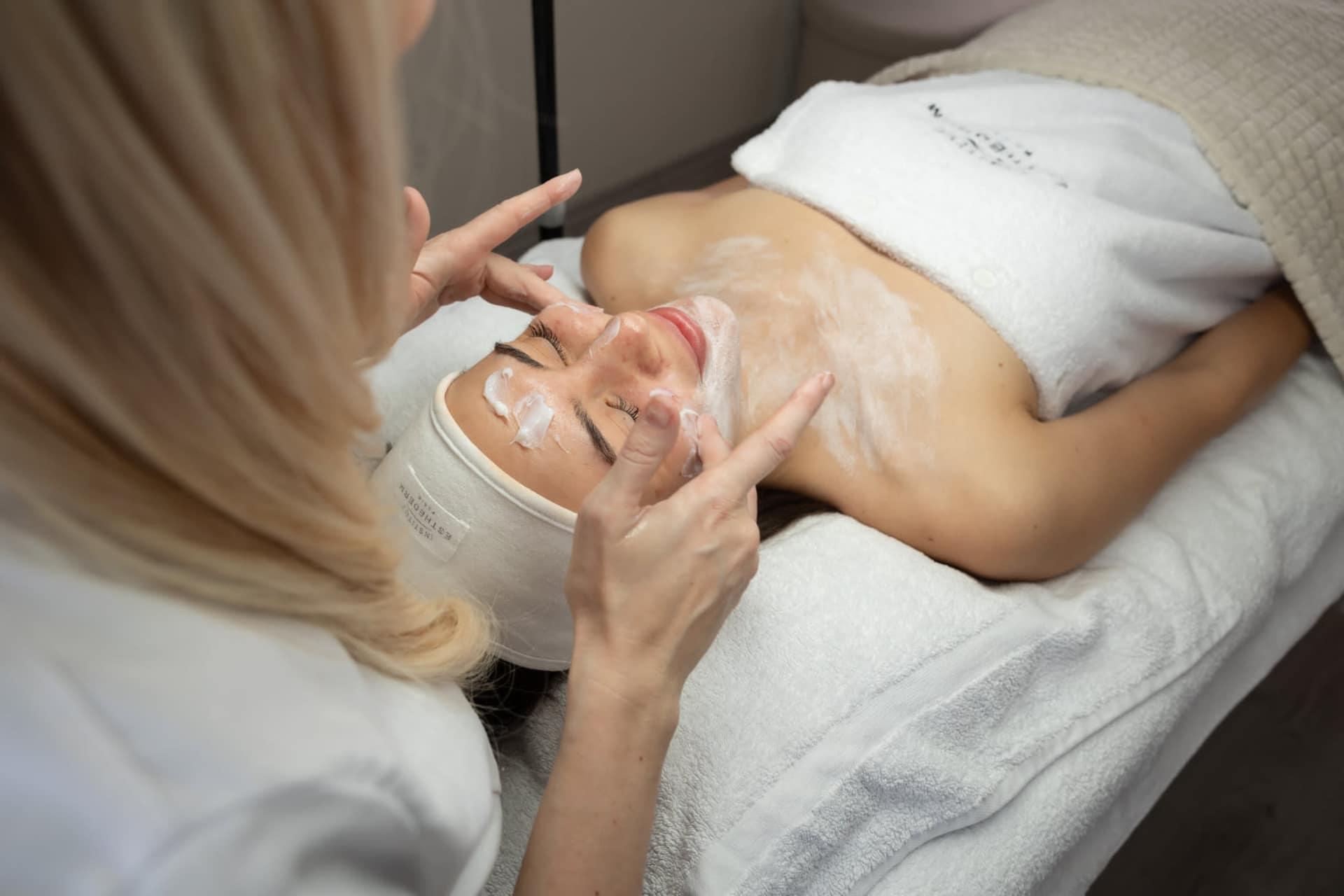 Kozmetička nanáša krém na tvár a dekolt klientky počas ošetrenia Esthederm.